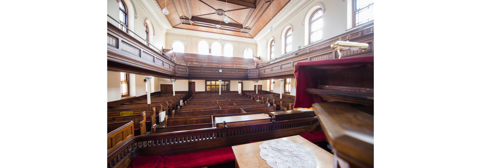 An image of the inside of Morah Chapel from the stage. There are many rows of wooden pews and a balcony from left to right.